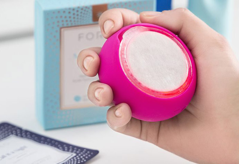 A hand holding a pink FOREO UFO led face mask device.
