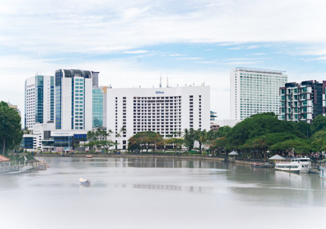A riverside view of modern Kuching featuring the Hilton hotel.