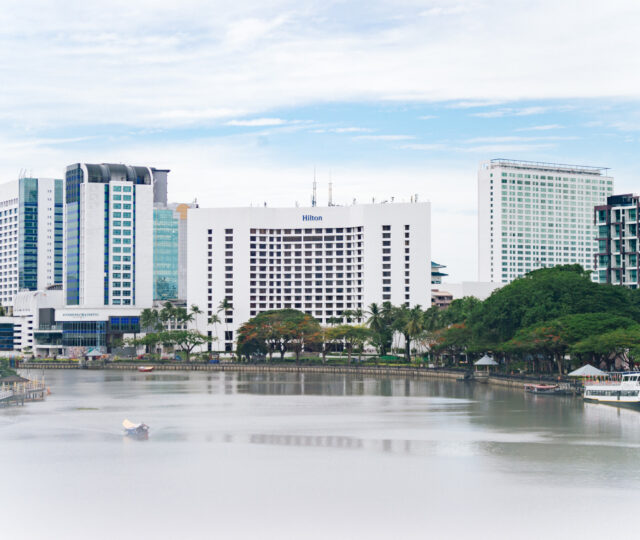 A riverside view of modern Kuching featuring the Hilton hotel.