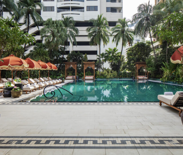 The 25-metre pool terrace at Anantara Siam Bangkok, with teak cabanas, palms and the city beyond.